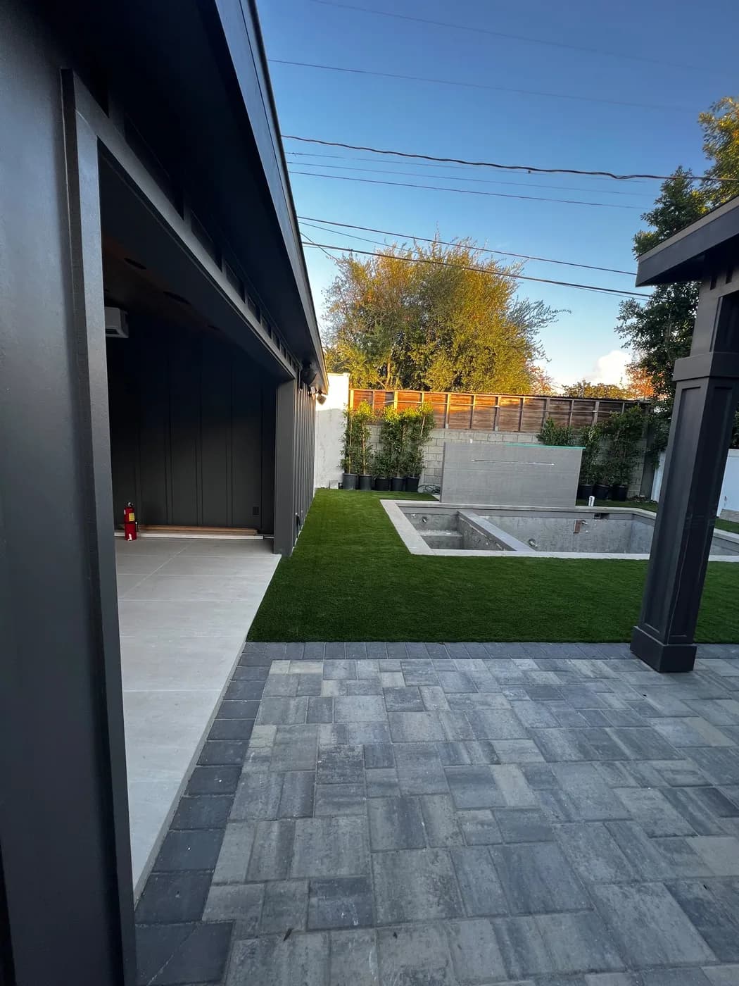 Paver patio with turf-lined joints leading to an in-ground pool and water feature wall