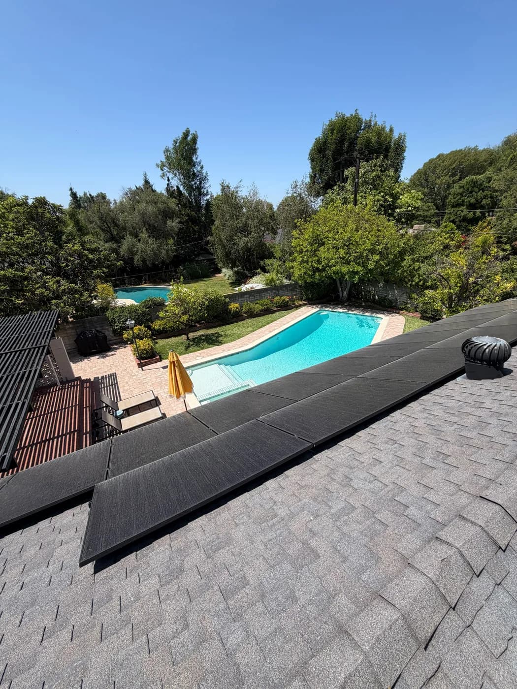 Solar panels installed on an asphalt shingle roof above a backyard pool