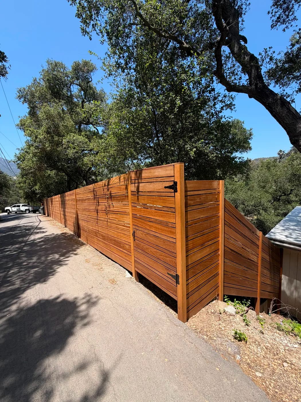 Long run of wood slat fence with gate by Top Tech Builders