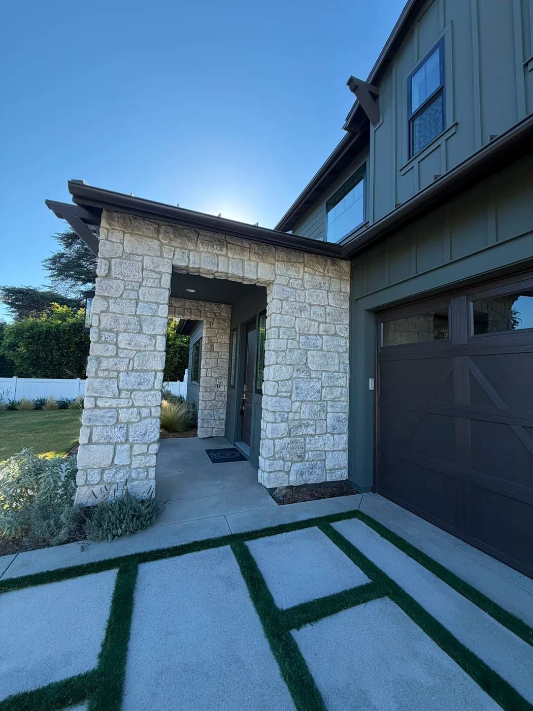 Stone entry archway with turf-inlaid paver walkway by Top Tech Builders