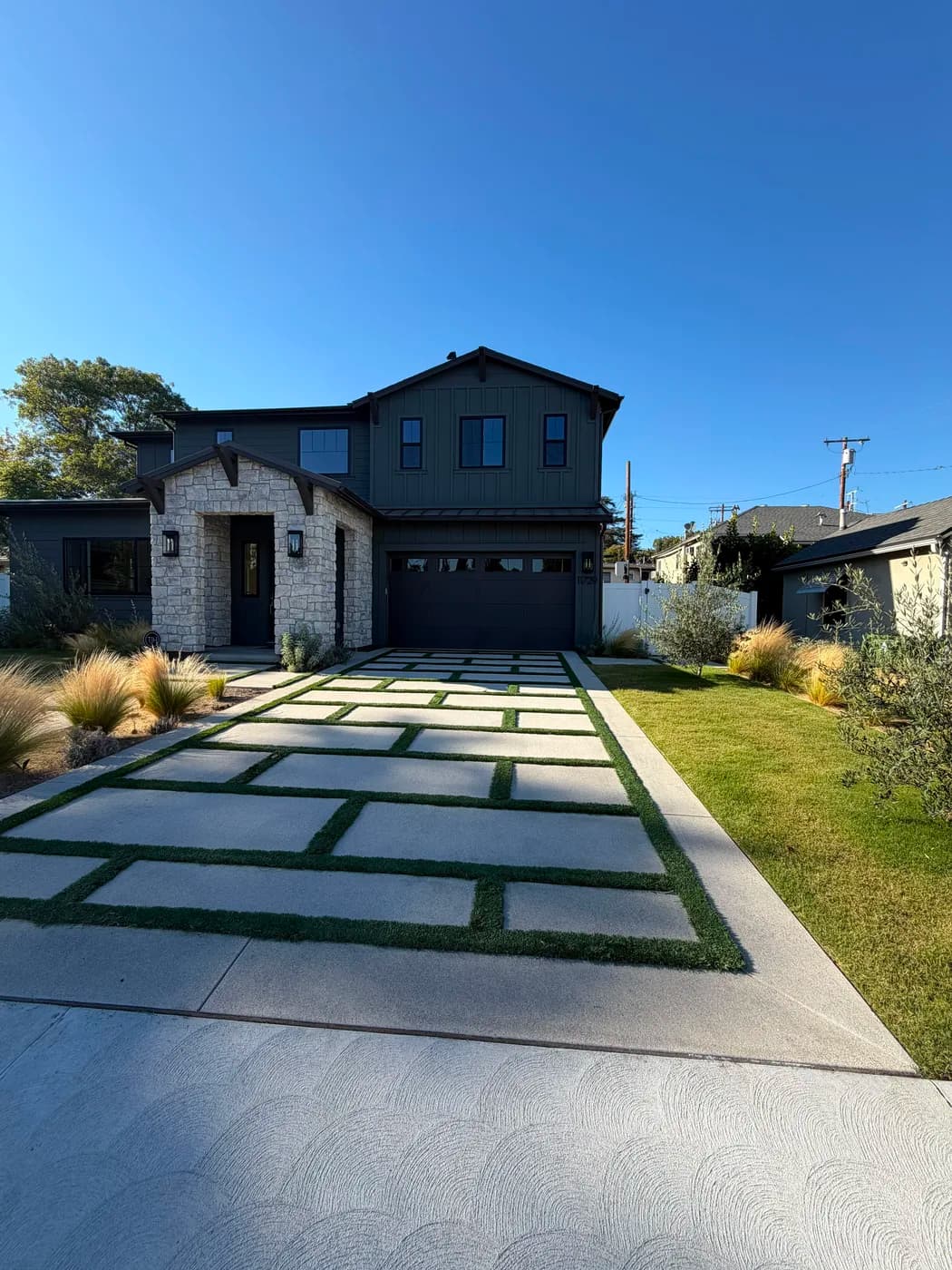 Turf-inlaid paver driveway leading to stone-and-board home exterior by Top Tech Builders