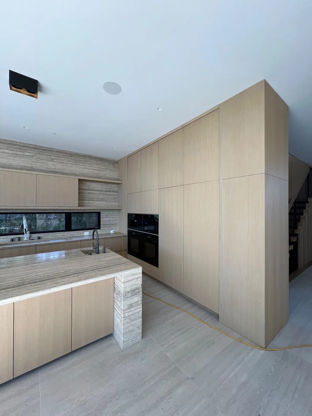 Full-height wood kitchen cabinetry wall with built-in double ovens