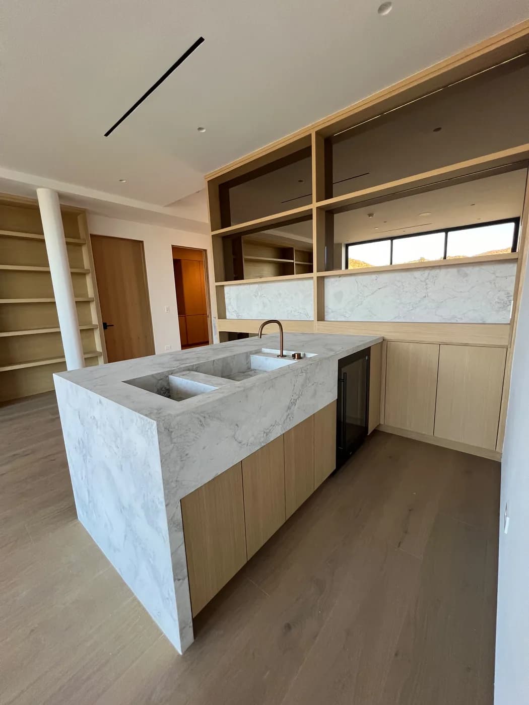 Wet bar with a waterfall marble island, built-in wine fridge, and open wood shelving